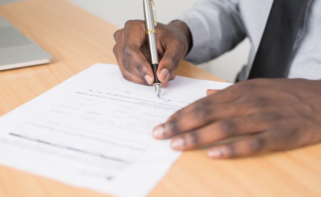Close-up of a businessman signing a contract at an office desk.